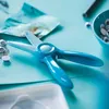 A close-up shot of turquoise children's scissors on a light blue surface, with craft supplies like googly eyes and paper visible. Náhled obrázku produktu