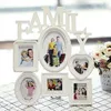 A white multi-photo frame collage with the word "FAMILY" above it, set against a checkered tablecloth and a blurred background with flowers. Produktbild-Vorschau