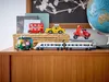 A collection of toy vehicles, including a train, bus, taxi, scooter, and auto-rickshaw, displayed on a wooden surface. Podgląd zdjęcia produktu
