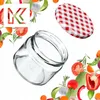 A glass jar and its lid are shown surrounded by fresh vegetables and herbs, with a stylized 'K' logo in the upper left corner. Anteprima dell’immagine prodotto