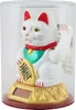 A white Maneki-neko cat figurine with a gold coin, sitting on a gold base with a solar panel, inside a clear plastic container. Produktbild-Vorschau
