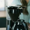 A close-up shot of a coffee maker's filter basket and water reservoir, with a person's hands visible in the background. Anteprima dell’immagine prodotto