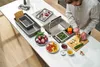 A person is preparing food in a kitchen, with various vegetables and kitchen accessories laid out on a white countertop. Voir les images du produit
