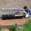 A boy is looking at a guinea pig cage outdoors. Náhľad obrázku produktu