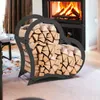 A heart-shaped metal log holder filled with firewood is placed in front of a fireplace with a fire burning. Podgląd zdjęcia produktu