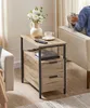 A side table with drawers next to a sofa, with a person sitting on the sofa and holding a remote control. Produktbild-Vorschau