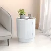 A white round side table with a fluted design sits next to a light gray armchair. A small potted plant and a glass of water on a book are on top of the table. Anteprima dell’immagine prodotto