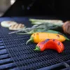 Schwarze Grillmatte aus Netz auf einem Holzkohlegrill, mit roten und gelben Paprika, Zwiebeln und Rosmarin beim Grillen Productafbeelding-voorbeeld