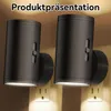 Two black plug-in night lights are shown plugged into wall outlets, illuminating the wall. Produktbild-Vorschau