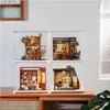 Four miniature dollhouse kits displayed in clear cases on a wooden surface. Podgląd zdjęcia produktu
