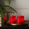 Four red LED candles are arranged on a gold tray, with a green pine branch in a gold pot to the left. Produktbild-Vorschau