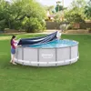 Two people are putting a cover on a round swimming pool in a backyard. Produktbild-Vorschau