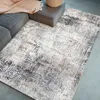 A modern abstract rug is placed on a floor next to a sofa and an ottoman. Produktbild-Vorschau