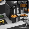 A black air fryer is shown on a kitchen counter, with food and ingredients around it. Produktbild-Vorschau