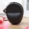 A black headphone case is displayed on a wooden surface, with some flowers and books in the background. Náhled obrázku produktu