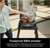 A person is using a black electric grill outdoors. Voir les images du produit