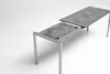 A modern extendable garden table with a grey stone-effect tabletop and silver metal legs, shown in an extended state against a white background. Produktbild-Vorschau