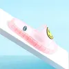 Pinke durchsichtige Rutsche-Sandale mit gelbem Smiley auf dem Riemen, auf weißer Oberfläche vor hellblauem Hintergrund Náhled obrázku produktu