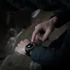 A person's hand is shown interacting with a smartwatch outdoors. Náhled obrázku produktu