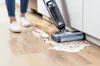 A person is using a wet vacuum cleaner to clean up a spill on a wooden floor. Voir les images du produit