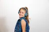 A young girl wearing headphones and a denim vest smiles at the camera. Produktbild-Vorschau