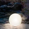 A glowing white sphere sits on a stone patio in a garden setting with rocks and lavender. Produktbild-Vorschau
