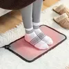 A person's feet wearing socks are standing on a heated foot mat on a fluffy rug. Slippers are visible in the background. Náhled obrázku produktu