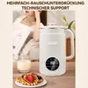 A soy milk maker is shown on a table next to a glass of milk and waffles, with a person reading in the background. Produktbild-Vorschau