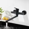 A black kitchen faucet mounted on a white wall above a sink, with water running. Produktbild-Vorschau