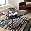 A black metal coffee table with books and a bowl of decorative items on it, placed on a striped rug in a living room setting with a brown leather sofa and stairs in the background. Produktbild-Vorschau