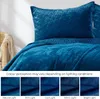 A close-up view of a quilted bedspread and pillow in a deep blue color, with a series of smaller images below demonstrating how the color perception changes under different lighting conditions. Produktbild-Vorschau
