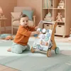 A baby is playing with a wooden walker in a nursery. Produktbild-Vorschau