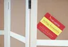 A red and yellow card with German text is attached to a corkboard, next to a light-colored wooden structure. Produktbild-Vorschau