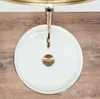 A top-down view of a white ceramic sink with a gold rim and a gold drain. Produktbild-Vorschau