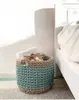 A woven basket filled with magazines and a towel sits next to a bed. Podgląd zdjęcia produktu