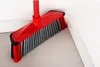 A red broom with gray bristles is positioned in the corner of a room, leaning against a white wall and baseboard, on a light wooden floor. Anteprima dell’immagine prodotto