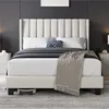A bed with a beige upholstered headboard and frame, dressed with white bedding, a dark gray blanket, and a decorative pillow. A robot vacuum cleaner is visible underneath the bed. Produktbild-Vorschau