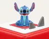 A blue Stitch figurine sits on a white surface with red and gray accents, against a plain white background. Anteprima dell’immagine prodotto