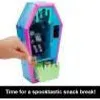 A hand is holding a coffin-shaped toy with a colorful, iridescent finish. The toy is open, revealing a miniature interior with some accessories. Green grass-like material is visible at the bottom. Anteprima dell’immagine prodotto