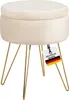 A beige upholstered stool with gold hairpin legs, featuring a tag with the German flag and text.