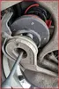 A close-up view of a car's suspension system, showing a spring and a tool being used. Produktbild-Vorschau
