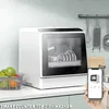 A countertop dishwasher is shown on a kitchen counter, with a smartphone displaying the dishwasher's interface in the foreground. Produktbild-Vorschau