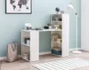 A white desk with integrated shelving units is shown in a room with light blue walls and a wooden floor. A floor lamp stands to the right of the desk, and a world map is hung on the wall above it. A tote bag is placed on the floor to the left of the desk. Anteprima dell’immagine prodotto