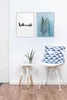 A minimalist interior scene with two framed pictures on a white wall, a small side table with a plant, and a chair with a patterned cushion. Podgląd zdjęcia produktu