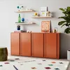 A modern living room with an orange cabinet, shelves with decor, a rug, and a plant. Voir les images du produit