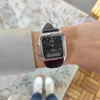 A person wearing a watch on their wrist, with their feet in white sneakers visible in the background. Produktbild-Vorschau