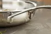 A close-up shot of the handle and rim of a stainless steel frying pan, resting on a marble countertop. Voir les images du produit