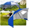 A woman relaxing on a beach chair under a blue and white beach umbrella, with a lake and mountains in the background. Another beach umbrella is in the foreground. Anteprima dell’immagine prodotto