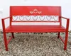 A red metal garden bench with heart-shaped decorative elements on the backrest, placed outdoors on a gravel surface. Produktbild-Vorschau