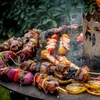 A close-up shot of various skewers of meat, shrimp, and vegetables being grilled on a large, round griddle. Náhled obrázku produktu